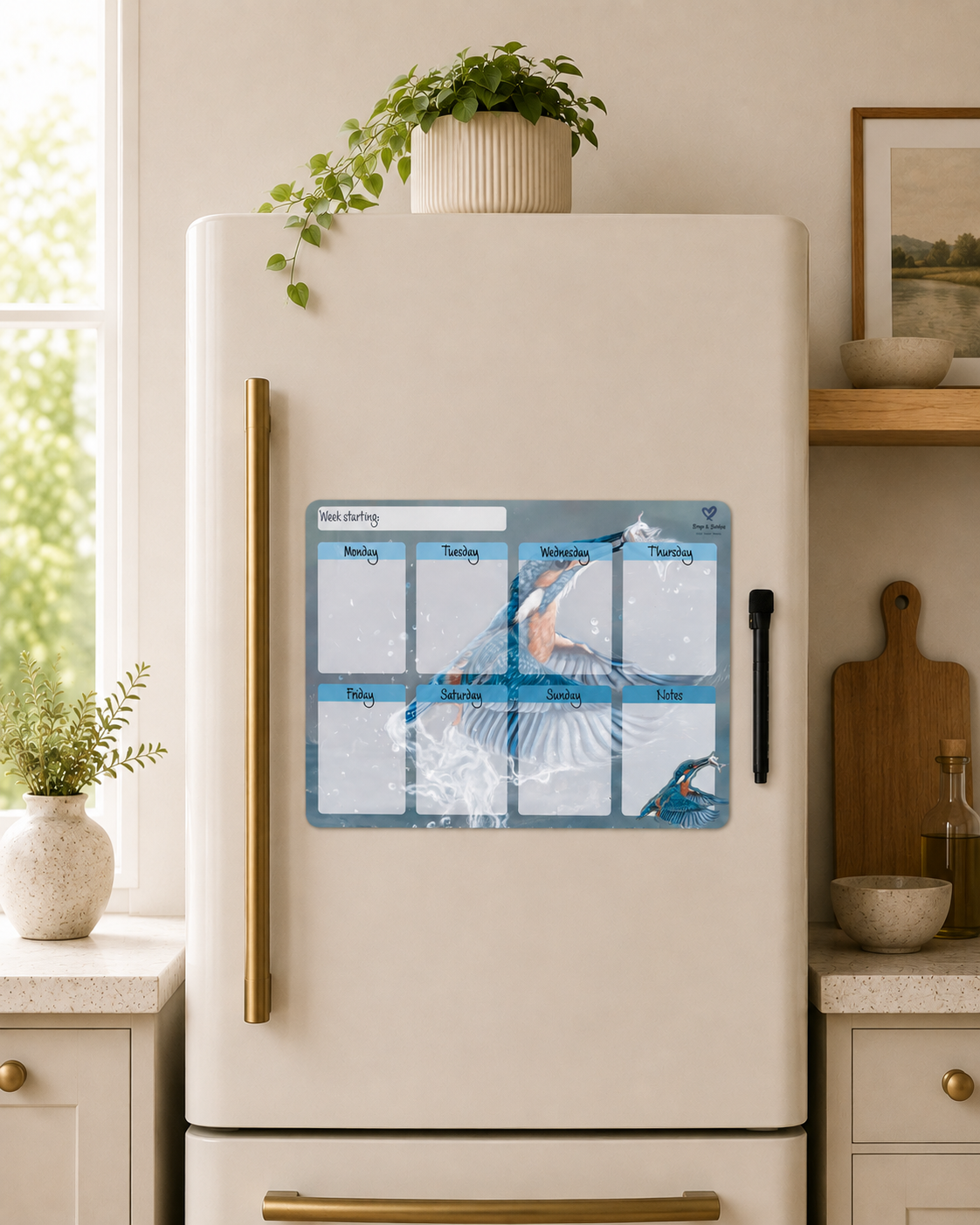 A weekly planner magnetic board with a Kingfisher  design, displayed on the front of a cream-colored refrigerator in a modern kitchen setting.
